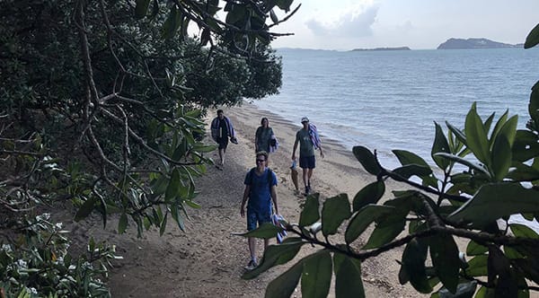 Photo of four people walking up the beach with the ocean in the background.