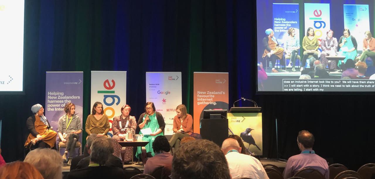 Photo of six people sitting on the stage addressing the audience